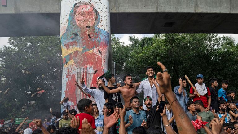 Protesters celebrate beside a defaced portrait of Ms Hasina.
Pic: Reuters/Fatima Tuj Johora