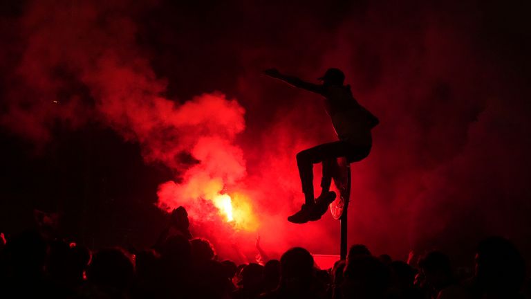 A PSG supporter on a traffic sign in Paris while red flares are set off after the team won the Champions League. Pic: AP